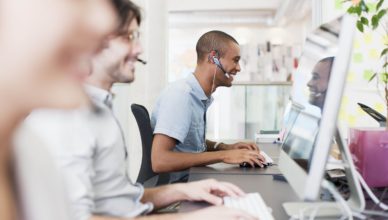 Menschen arbeiten in einem Büro und haben jeweils Headsets auf und blicken auf ihre Bildschirme.