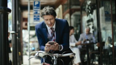 Ein Geschäftsmann schaut auf sein Mobiltelefon während er sich in einer städtischen Umgebung befindet.